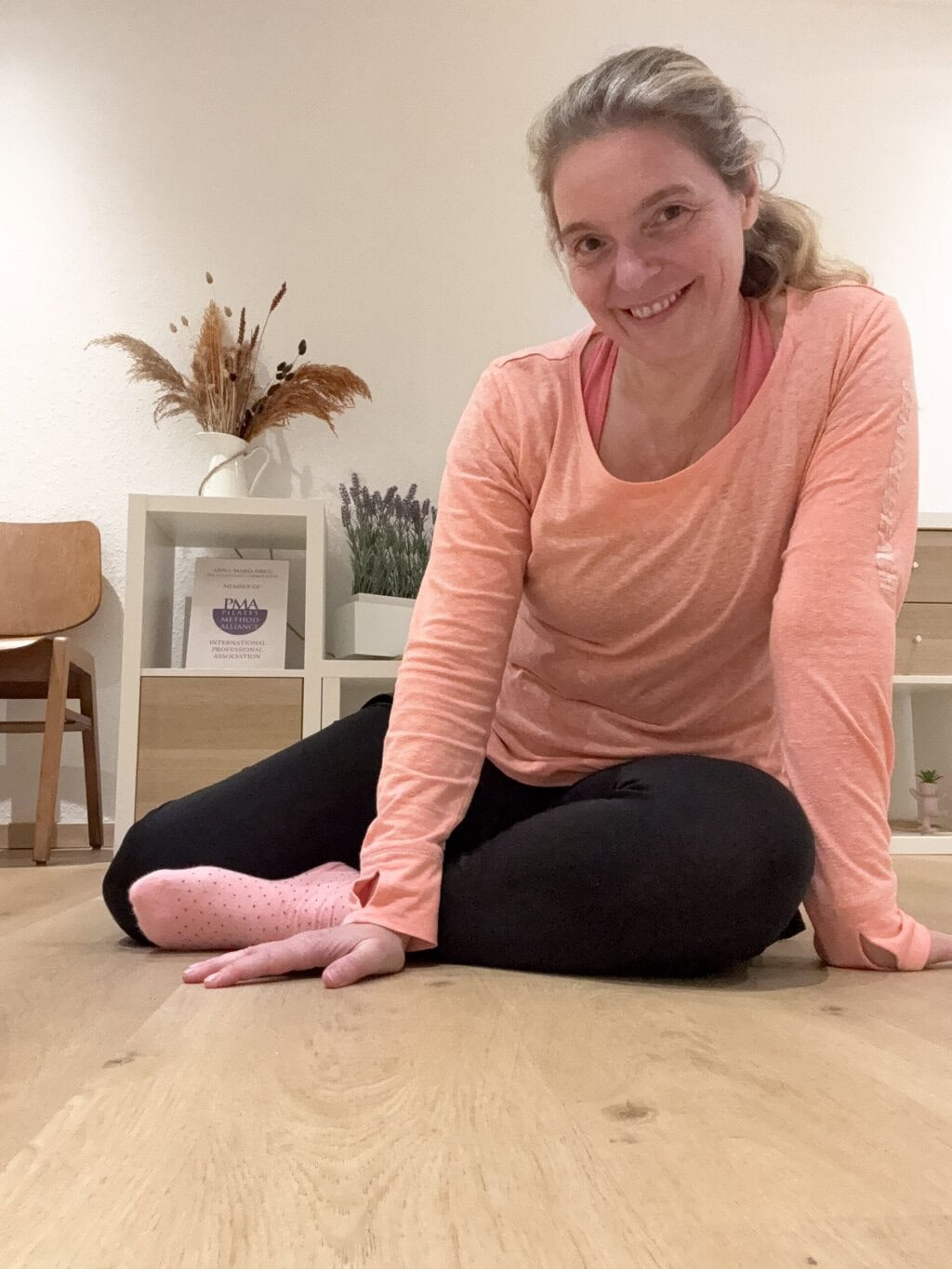 Pilates Anna sitzt im Pilatesstudio im im Vorraum auf dem Boden